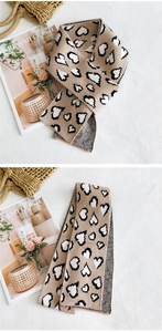 Dettaglio della trama a maglia di una sciarpa beige con motivi a cuore e decori