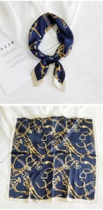 Détail d'un foulard en soie bleu marine avec chaîne équestre dorée et bordure blanc cassé