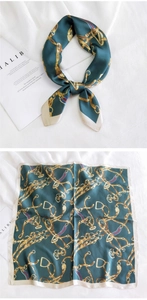 Détail d'un foulard en soie verte avec imprimé chaîne dorée et mors de cheval