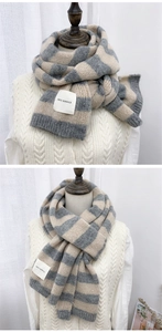 Detail showing grey and beige striped knit texture and square brand patch on the winter scarf