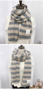 Detail of gray and beige striped knit scarf featuring a soft fabric texture and stitched label