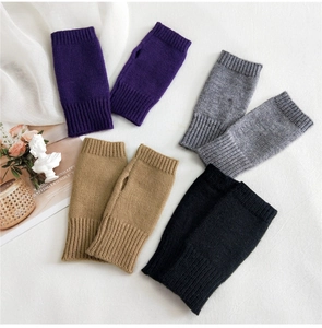 Detail of knitted fingerless gloves in purple, grey, camel, and black on a white desk