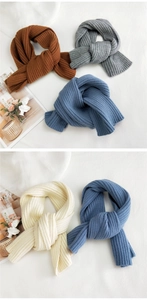 Close-up of thick ribbed knit scarves in caramel, grey, and blue on a white surface