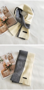 Close-up of gray and white knitted scarf with leather brand tag and soft knit texture