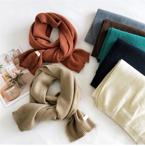 Detailed overhead view of multiple solid color knit scarves with ribbed edges and fabric tags