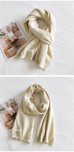 Detail view of cream knit scarf with ribbed edges and minimalist label on linen background