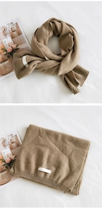 Detailed close-up of thick camel knit scarf featuring ribbed texture and white label detail