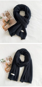 Detail of black thick knitted scarf featuring vertical ribbed patterns and minimalist label