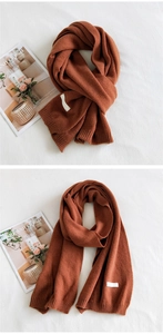 Close-up of rust red knit scarf featuring thick vertical ribbing and white woven label
