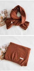 Close-up of rust red knit scarf featuring ribbed edges and a minimalist fabric label
