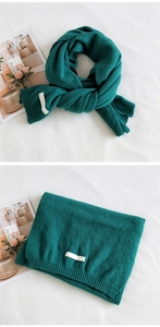 Detail of dark green knit scarf showing ribbed texture and decorative white woven label