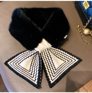 Detail of cross-knot knitted scarf with black faux fur trim on leather surface