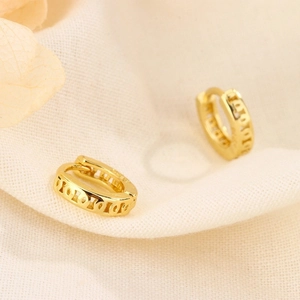 Detailed close-up of gold geometric hollow hoop earrings on a soft textured fabric background