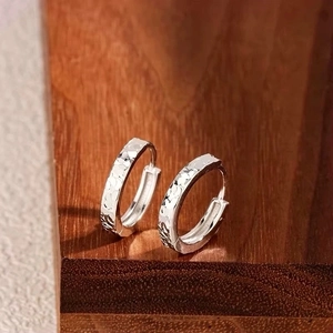 Elegant silver textured hoop earrings with hammered finish on a dark wooden surface