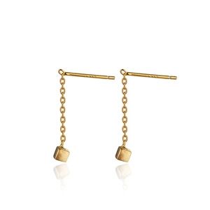Macro detail of gold-plated geometric cube earrings with brushed finish and long chain link