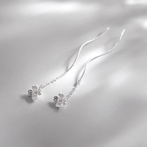 Silver flower tassel drop earrings with long chain and textured petals on a grey background