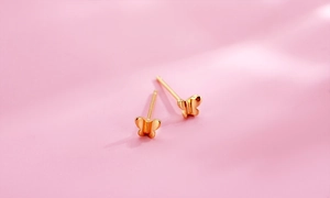 Gros plan de boucles d'oreilles papillon en or jaune poli sur fond de satin rose clair