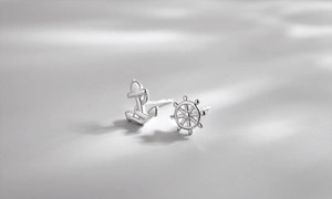 Macro shot of silver asymmetrical earrings featuring anchor and ship wheel nautical designs