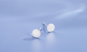 Macro shot of minimalist silver round stud earrings on a serene light blue background
