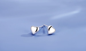 Close-up of polished silver heart stud earrings on a soft lavender background