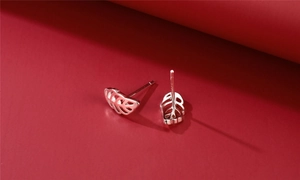 Detailed view of leaf-shaped cutout silver earrings on a deep red elegant backdrop