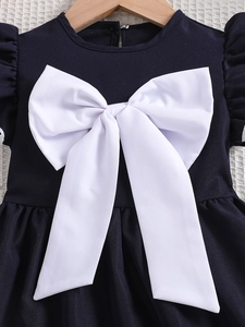 Marineblauwe meisjesjurk met een grote witte strik en ruchesmouwen aan een hanger
