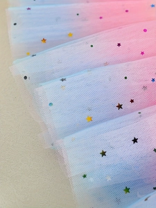 Close-up of rainbow sequin tulle fabric with star patterns and pink-blue gradient mesh