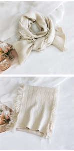 Gros plan sur le tricot à losanges et les longs pompons de l'écharpe blanc crème