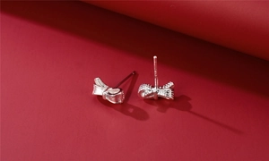 Macro detail of S925 sterling silver bow earrings with textured surface on dark red background