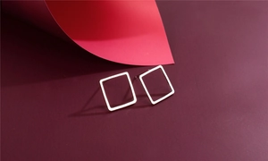Detail of geometric square hollow earrings in polished silver on artistic backdrop