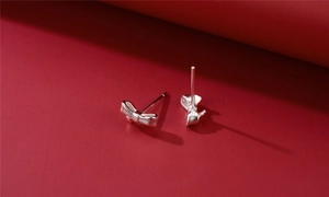 Macro shot of 925 sterling silver bow knot stud earrings on a dark red background