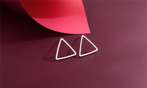 Macro shot of polished silver geometric triangle stud earrings on a dark red background
