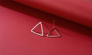 Detail view of hollow triangle stud earrings in polished silver on a deep red background