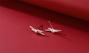 Macro shot of minimalist silver knot earrings with a polished finish on red surface