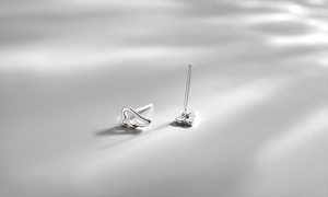 Macro shot of silver angel wing stud earrings with hollow design on soft gray background