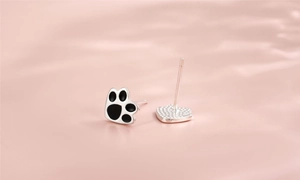 Macro shot of silver cat paw stud earrings with black enamel detail on pink silk