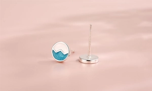 Detailed view of silver wave pattern earrings with blue enamel finish on pink background
