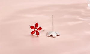 Macro view of red enamel flower earrings with S925 silver studs on pink background