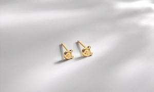 Close-up of minimalist golden bear studs with a high-polished finish on grey texture
