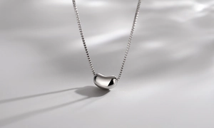 Macro detail of high-polish silver bean pendant on a delicate box chain necklace