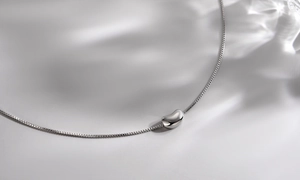 Macro view of polished silver bean pendant with sleek box chain on a soft grey background