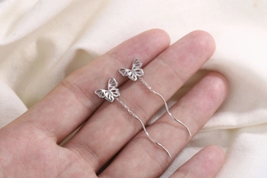 Détail de boucles d'oreilles papillon en argent avec de fines chaînes en vague à la main