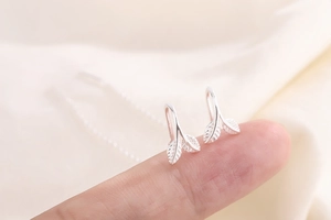 Macro shot of S925 sterling silver leaf tassel earrings held on a fingertip
