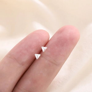 Minimalist silver triangle stud earrings shown on fingertip for size reference