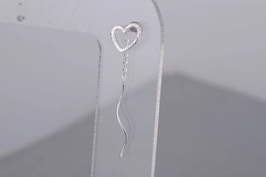 Detail of silver heart tassel earrings featuring hollow heart stud and wavy metal wire