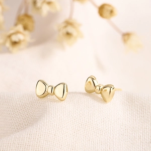 Elegant gold bow-shaped stud earrings with a polished finish on white textured fabric