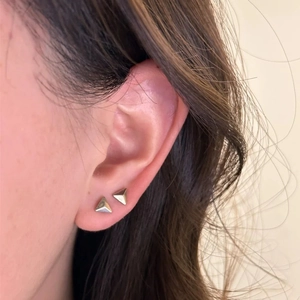 Minimalist silver triangle pyramid stud earrings shown on ear with a polished mirror finish