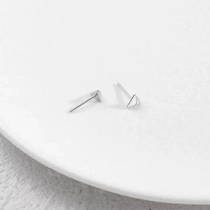 Minimalist geometric triangle stud earrings in polished silver on a ceramic tray