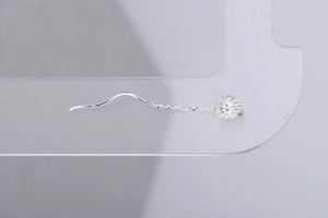 Close-up of silver drop threader earring with wavy hook and textured sphere pendant