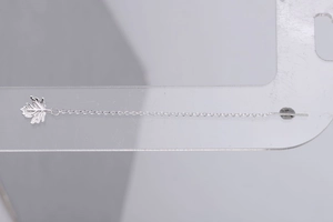 Close-up of a silver maple leaf tassel earring on a transparent acrylic display stand